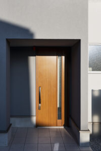 The entrance of a minimalist home with a sleek, wooden contemporary door set within a clean-lined, shadow-cast facade, embodying modern elegance and simplicity.